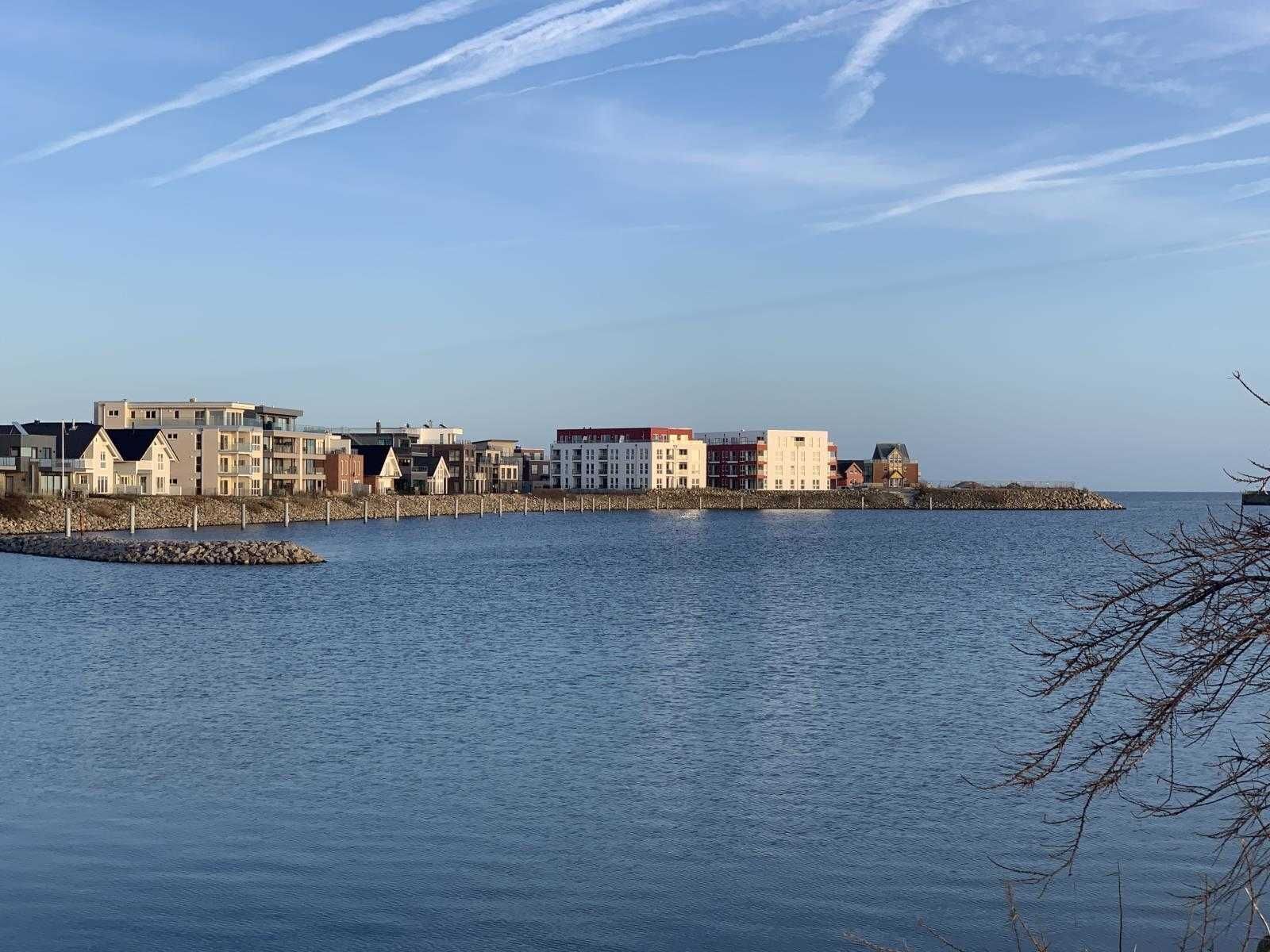 Rantakiinteistö, jossa on rivi rakennuksia rannan varrella, kivinen aallonmurtaja ja kirkas taivas.