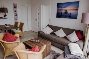 Uma sala de estar com sofá, cadeiras, mesa de centro e um quadro de um cais.