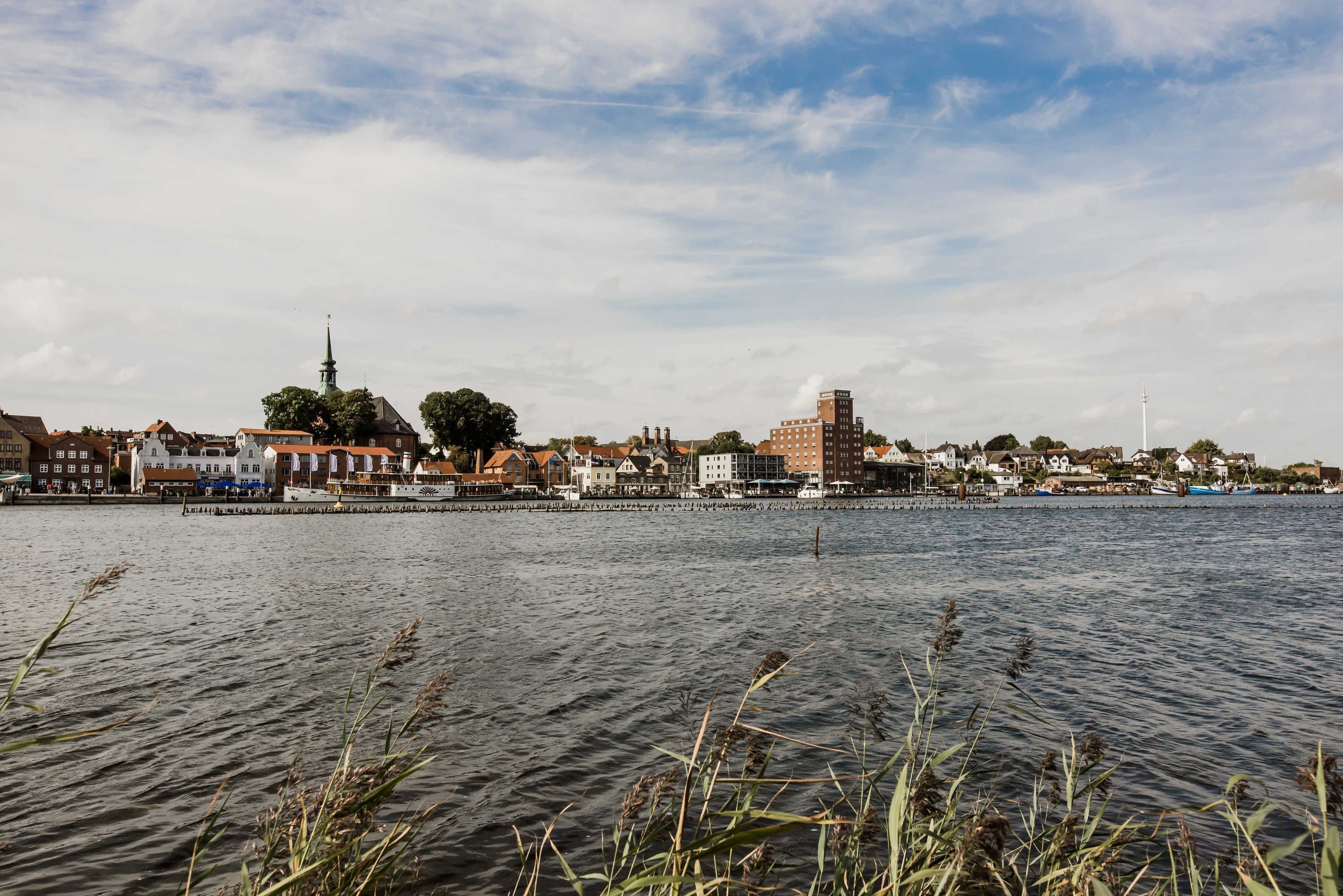 A waterfront cityscape with buildings, a church spire, and a bridge.