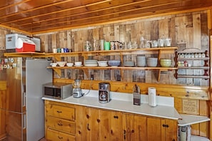 A kitchen with wooden cabinets, a refrigerator, a microwave, a coffee maker, and various kitchen utensils. - Rustic Lakefront! PET FRIENDLY! Boat Dock! Pool Table! HOT TUB! (Big Bear Lake)