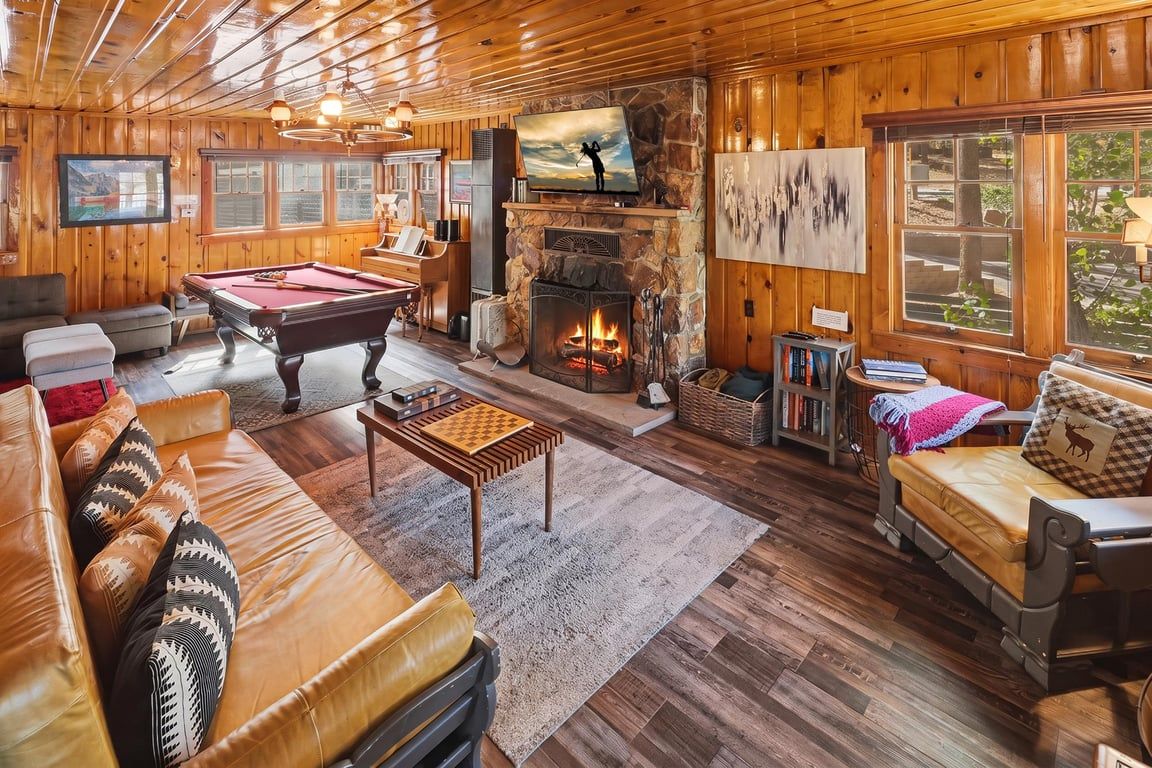 A cozy lodge interior with a pool table, leather sofa, fireplace, and wooden walls.