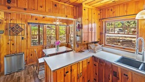 Interior d'una cabana de fusta amb zona de cuina, incloent-hi un rentapeus, armaris i una taula de dinar amb cadires.