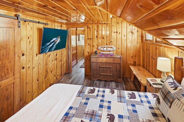 L’intérieur d’une cabane en bois comprend un lit, un banc, une commode et un téléviseur fixé au mur.