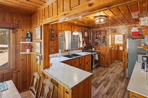 A wooden cabin interior with a kitchen featuring a central island, a dining area, and a visible window. - Rustic Lakefront! PET FRIENDLY! Boat Dock! Pool Table! HOT TUB! (Big Bear Lake)