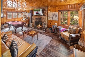 Un intérieur chaleureux et accueillant, avec une table de billard, un canapé en cuir, une cheminée et de grandes fenêtres.