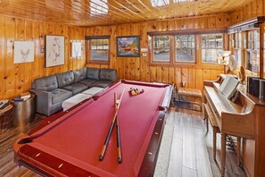 A pool table with cues, a sofa, and a piano in a room with wooden walls and windows. - Rustic Lakefront! PET FRIENDLY! Boat Dock! Pool Table! HOT TUB! (Big Bear Lake)