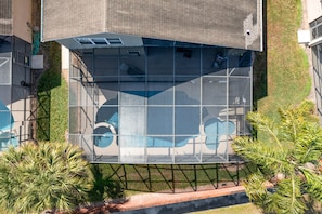 Um edifício moderno com fachada de vidro, piscina no terraço e áreas verdes ao redor.