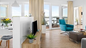 A modern living room with a flat-screen TV, a blue armchair, and a dining area with a table set for two.