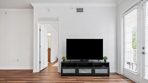 A modern living room with a flat-screen TV on a black entertainment unit, wooden flooring, and white walls.