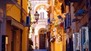 A narrow street with buildings on either side, a clock tower in the background, and a staircase leading up to a door. - Agora Apartments Casetta Sorrentina (Sorrento)