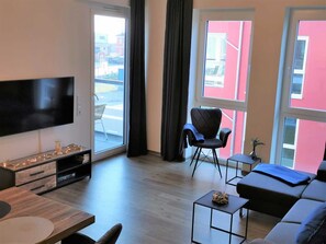 Uma sala de estar moderna com televisão de tela plana, um sofá, uma poltrona e uma pequena mesa.