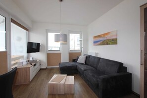 Uma sala de estar moderna com um sofá seccional cinza escuro, uma mesa de centro de madeira, uma TV de tela plana e um quadro de uma paisagem na parede.