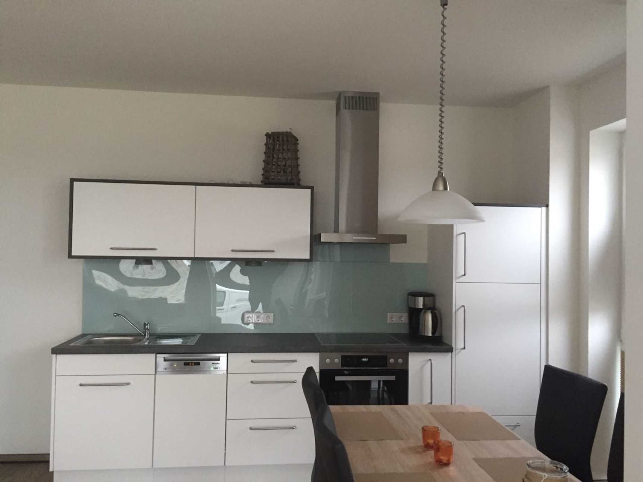 A modern kitchen with white cabinets, a stainless steel range hood, and a coffee maker.