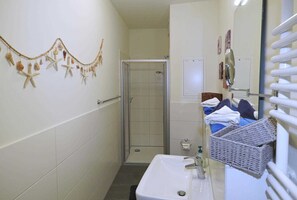 Ein Badezimmer mit Dusche, Waschbecken und Spiegel. Ein Handtuchhalter mit Handtüchern und einem Korb.
