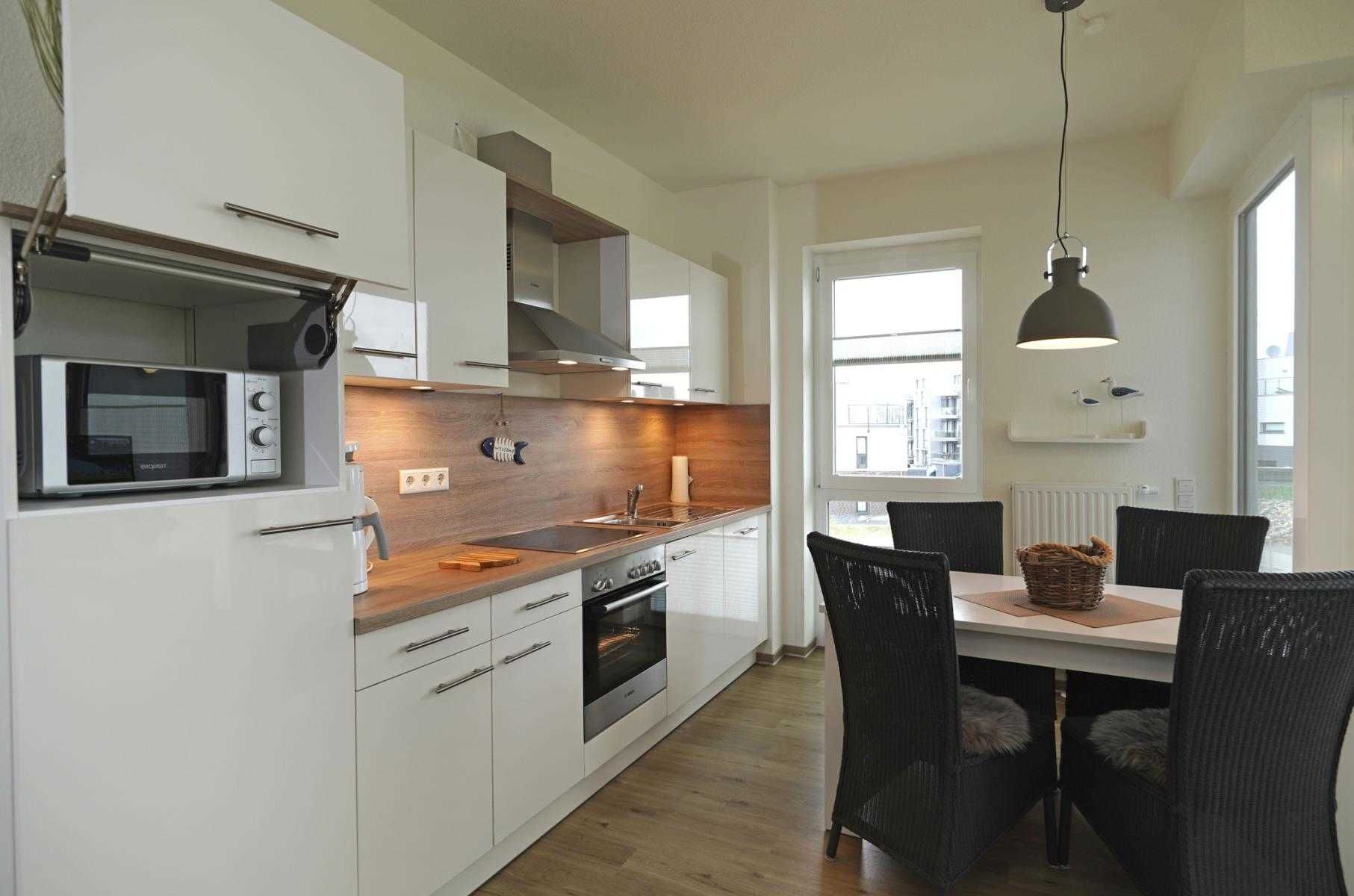 A modern kitchen with white cabinets, a microwave, a stove, and a dining area with a table and chairs.