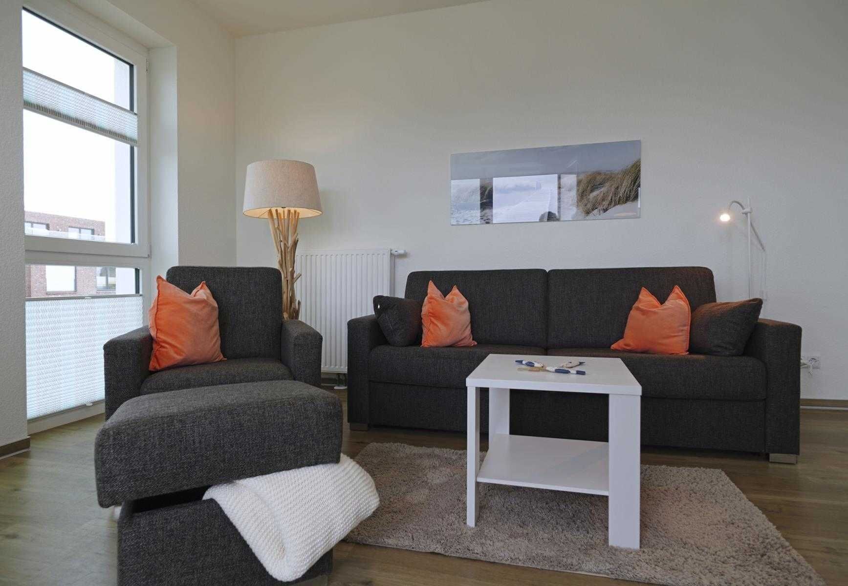 Un salon avec un canapé gris, deux coussins orange, une table basse blanche et un lampadaire.