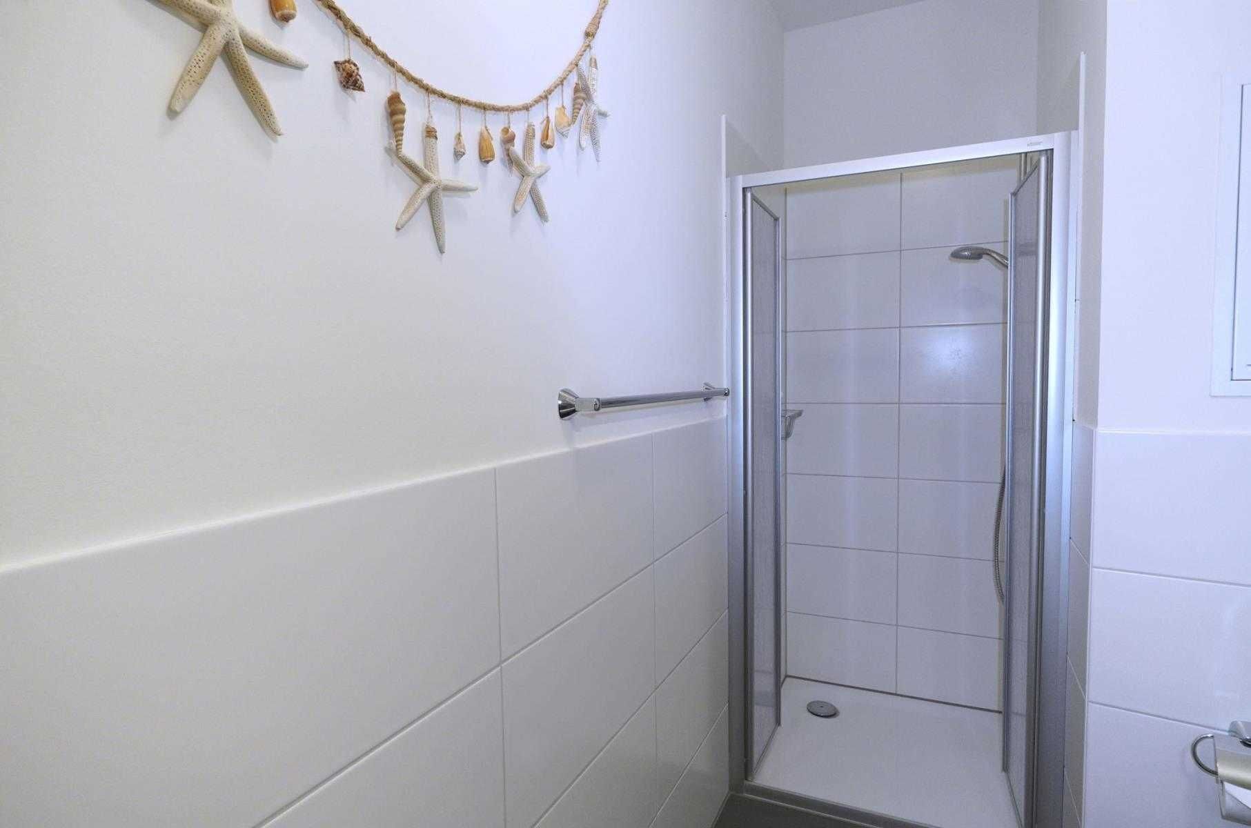 A bathroom with white tiles, a glass shower enclosure, and a starfish wall decoration.
