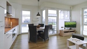 Un appartement moderne comprenant une cuisine, un coin repas et un salon. Il est doté de grandes fenêtres, d’un téléviseur à écran plat et d’une table à manger avec des chaises.