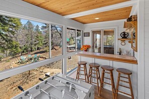 A kitchen with a bar area, large windows, and a view of the outdoors. - Central A/C! HOT TUB! Play on an Acre! Near Bear Mountain/Zoo/Golf/Hiking! EV Charger! Multi-Game Tables! (Big Bear City)