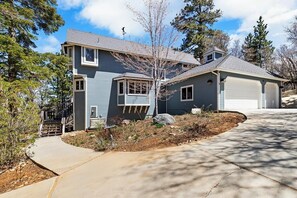 A two-story house with a garage, a covered driveway, and a landscaped front yard. - Central A/C! HOT TUB! Play on an Acre! Near Bear Mountain/Zoo/Golf/Hiking! EV Charger! Multi-Game Tables! (Big Bear City)