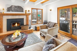 A cozy living room with a fireplace, a comfortable sofa, a coffee table, and a view of the outdoors through a sliding glass door.