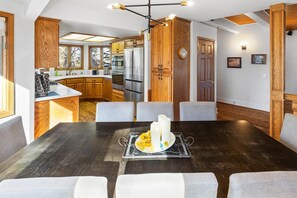 A modern kitchen with wooden cabinets, stainless steel appliances, and a dining area with a dark wooden table and grey upholstered chairs.
