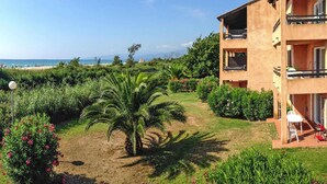 Ein zweigeschossiges Gebäude mit Balkonen, einem Garten mit Palmen und Blick auf den Strand.