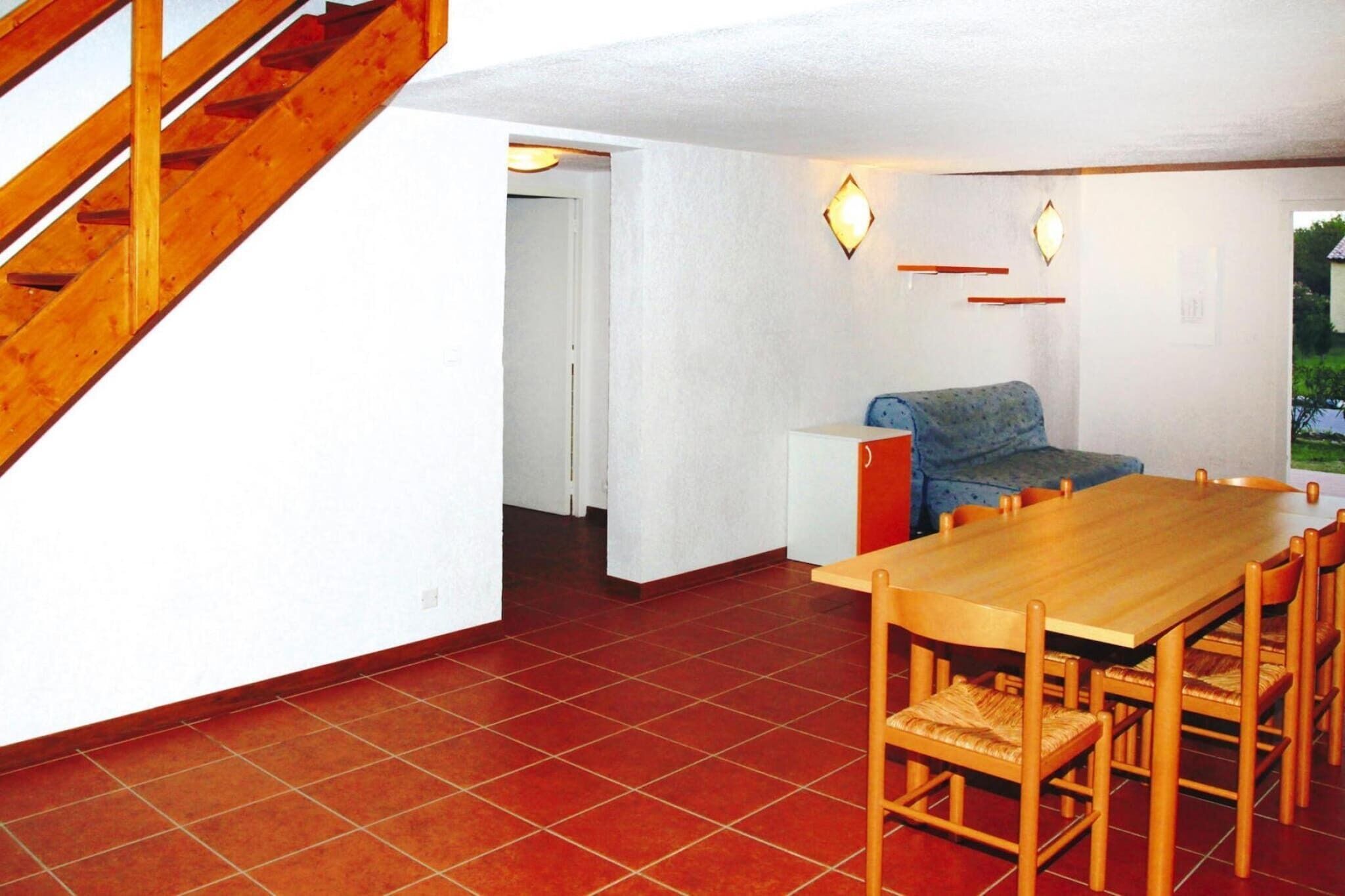 A dining area with a wooden table and chairs, a sofa, and a staircase.