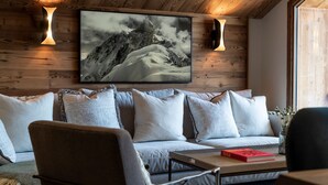 A cozy living room with a wooden ceiling, a large framed mountain landscape, a sofa with patterned cushions, and a coffee table with a book. - 4-bedroom duplex in Méribel, near center and slopes, with concierge services (Méribel)