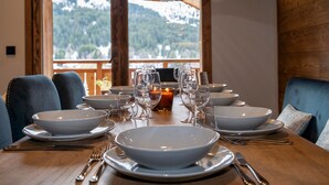 A dining table set with white plates, bowls, and glasses, with a candle and a decorative light fixture above. - 4-bedroom duplex in Méribel, near center and slopes, with concierge services (Méribel)