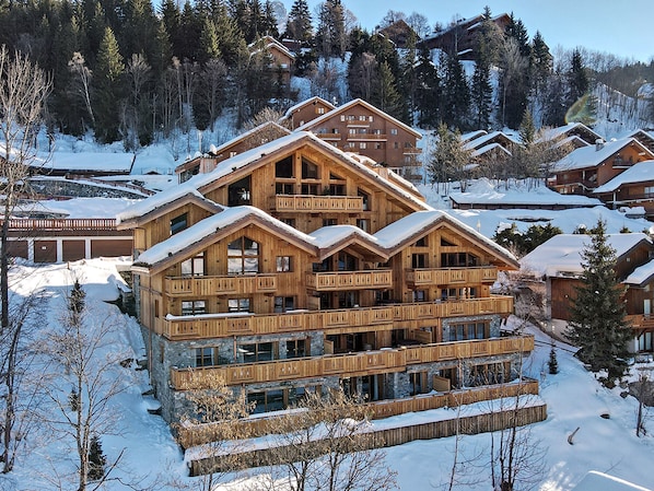 A multi-story wooden lodge with balconies, surrounded by snow-covered trees and other lodges.