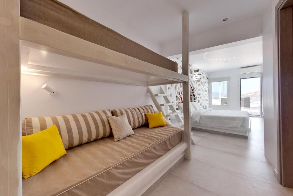 A modern bedroom with a sofa bed, a white headboard, and a view of the outdoors.