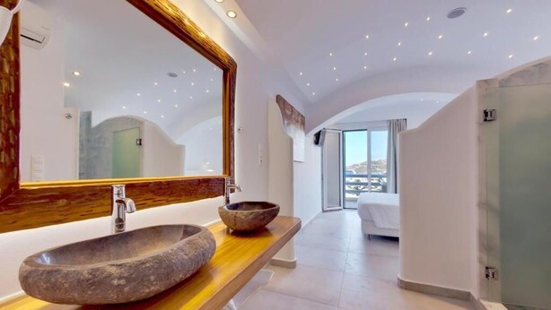 A modern bathroom with a large stone sink, a wooden vanity, and a large mirror. - Ibiscus Boutique Hotel (Mykonos)
