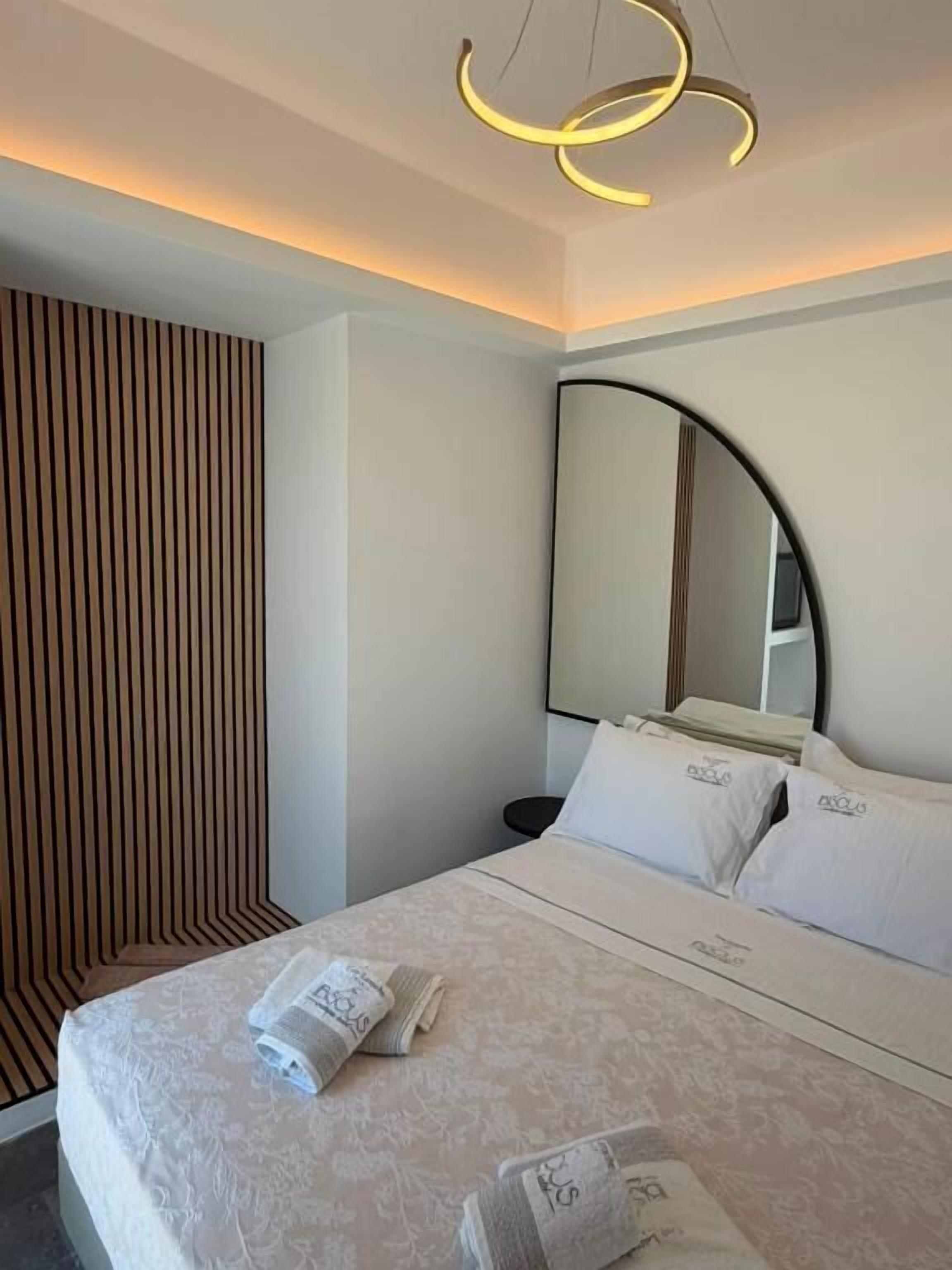 A modern hotel room with a bed, a large mirror, and a unique ceiling light fixture.