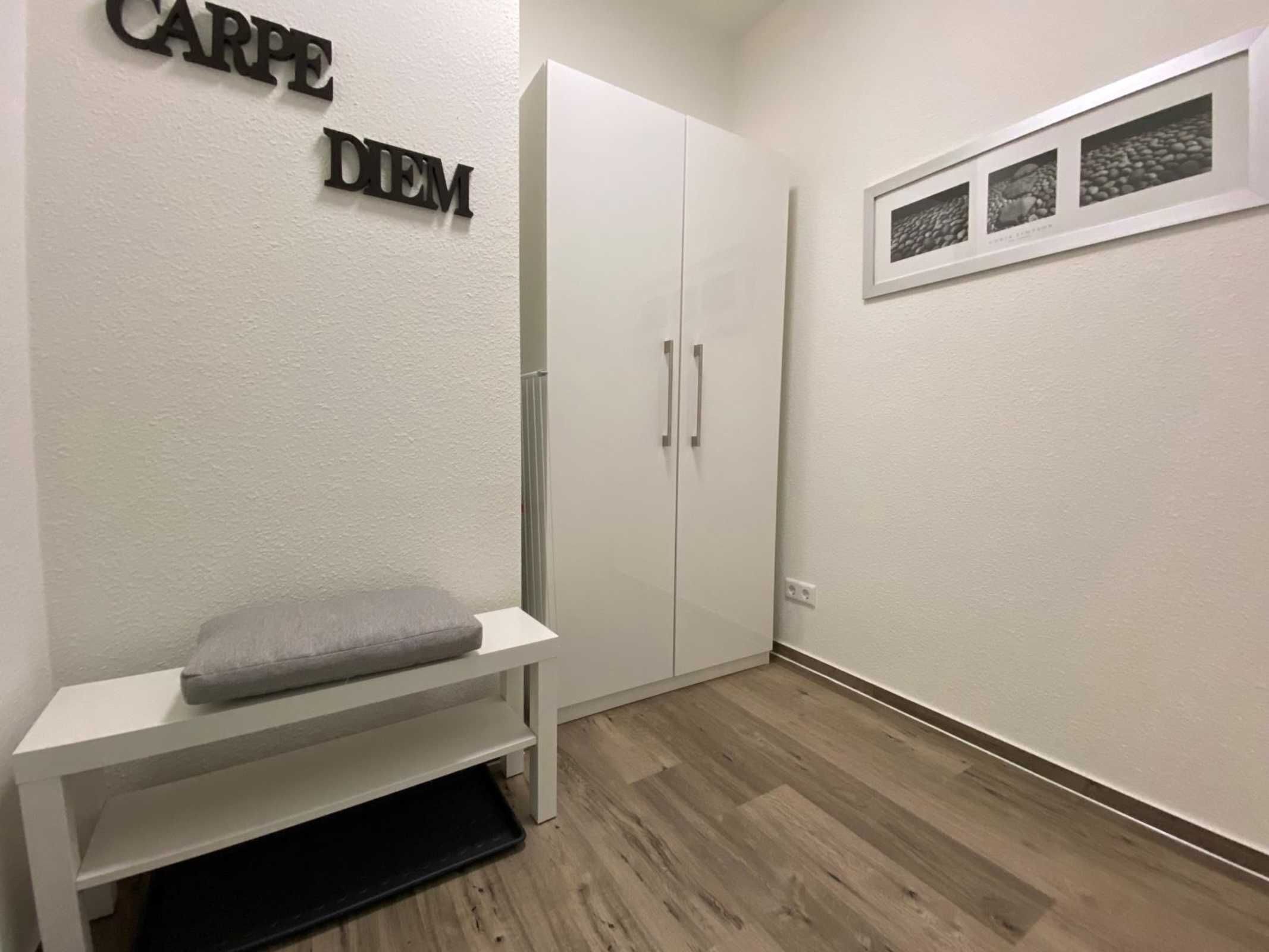 Una habitación con un armario blanco, un banco con cojín y un estante de pared con cuadros enmarcados.