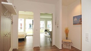 A hallway with wooden flooring, a bed in the background, a small bench, and a poster on the wall. - BOW-2.02, 4 pers., 55-65sqm (H) - Residence Bollwark 2.0 (Kappeln)