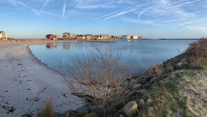 A coastal area with a sandy beach, a calm body of water, and a row of buildings in the background. - BOW-2.02, 4 pers., 55-65sqm (H) - Residence Bollwark 2.0 (Kappeln)
