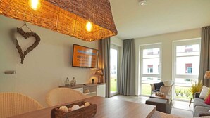 A modern living room with a wooden dining table, wicker ceiling light, and a TV mounted on the wall. - BOW-2.03, 4 pers., 55-65sqm (H) - Residence Bollwark 2.0 (Kappeln)