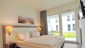 A hotel room with a large bed, a nightstand, a wall-mounted TV, and a sliding glass door leading to an outdoor area. - BOW-2.03, 4 pers., 55-65sqm (H) - Residence Bollwark 2.0 (Kappeln)