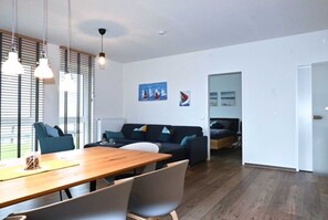 Un salon moderne avec une table à manger en bois, des chaises grises, un canapé bleu foncé agrémenté de coussins et un plancher en bois.