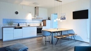 Een moderne keuken met witte kasten, een eethoek met een houten tafel en stoelen, en een flatscreen televisie aan de wand.