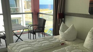 Een hotelkamer met een bed, een stoel en uitzicht op zee door een groot raam.