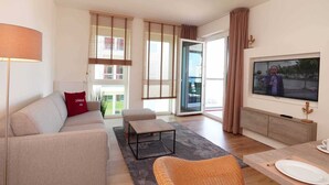 Een moderne woonkamer met een bank, een salontafel, een televisie en een eethoek met een tafel en stoelen.