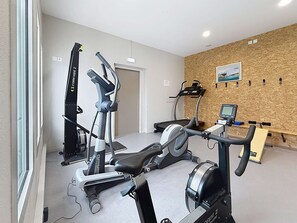 A gym with cardio machines, a rowing machine, and a wall-mounted TV. - Comfortable 2-Bedroom Mobile Home, 200m from Beach, Pool, WiFi, Parking (Jullouville)