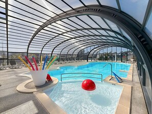A swimming pool with a glass ceiling, lounge chairs, and a red water feature. - Comfortable 2-Bedroom Mobile Home, 200m from Beach, Pool, WiFi, Parking (Jullouville)