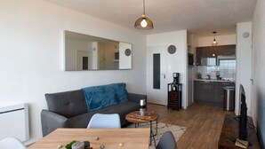 Ett modernt vardagsrum med en soffa, ett matbord och ett köksområde i bakgrunden.
