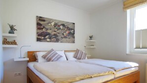 A bedroom with a wooden bed, white bedding, a painting of rocks, and two bedside tables with decorative items.