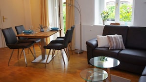 A modern living room with a dining area, a black leather sofa, a glass coffee table, and a dining table with chairs.