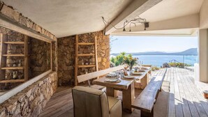An outdoor dining area with stone walls and wooden furniture overlooking a body of water.