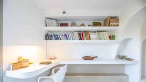 A modern, minimalist room with a white desk, a white chair, and shelves above containing books and decorative items.